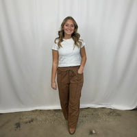 Woman wearing a white top and brown pants against a plain background